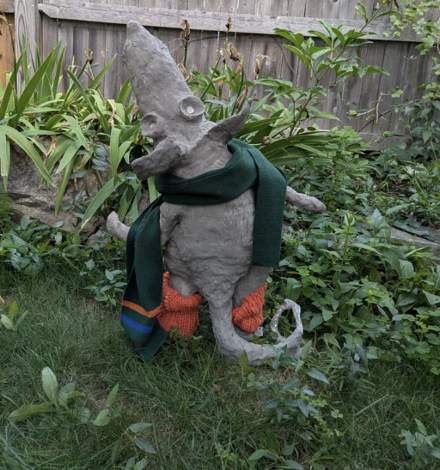 Sculpted rat in a green scarf, standing in a garden