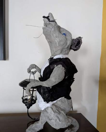 Sculpted rat in a black waistcoat carrying a lantern